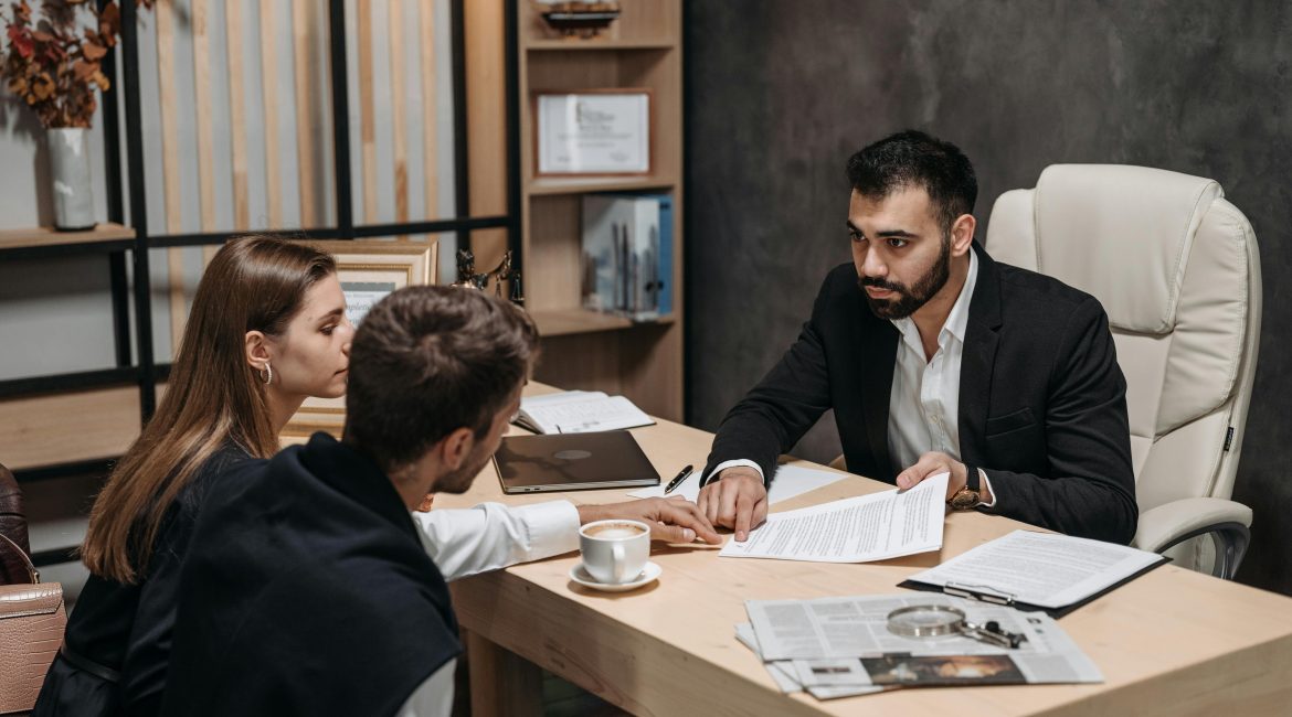 Abogado reunido con una pareja en su despacho, ofreciendo asesoramiento legal y revisión de documentos.