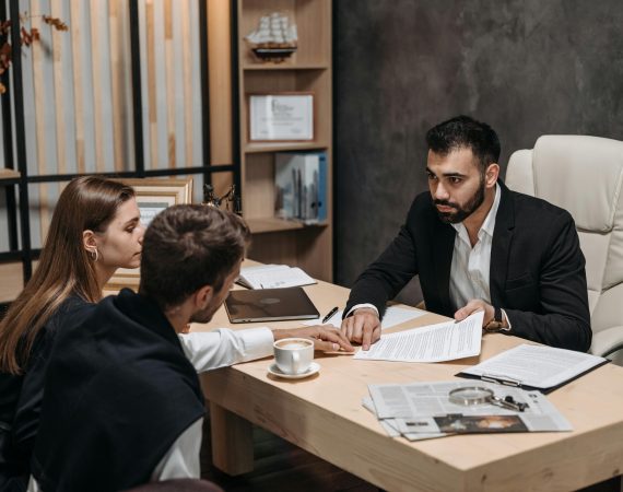 Abogado reunido con una pareja en su despacho, ofreciendo asesoramiento legal y revisión de documentos.