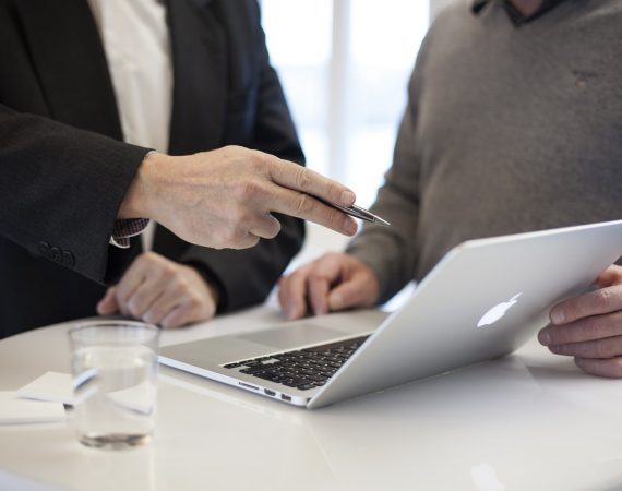 Dos hombres en una reunión de consultoría revisando documentos en un ordenador portátil, simbolizando servicios de asesoría legal profesional.