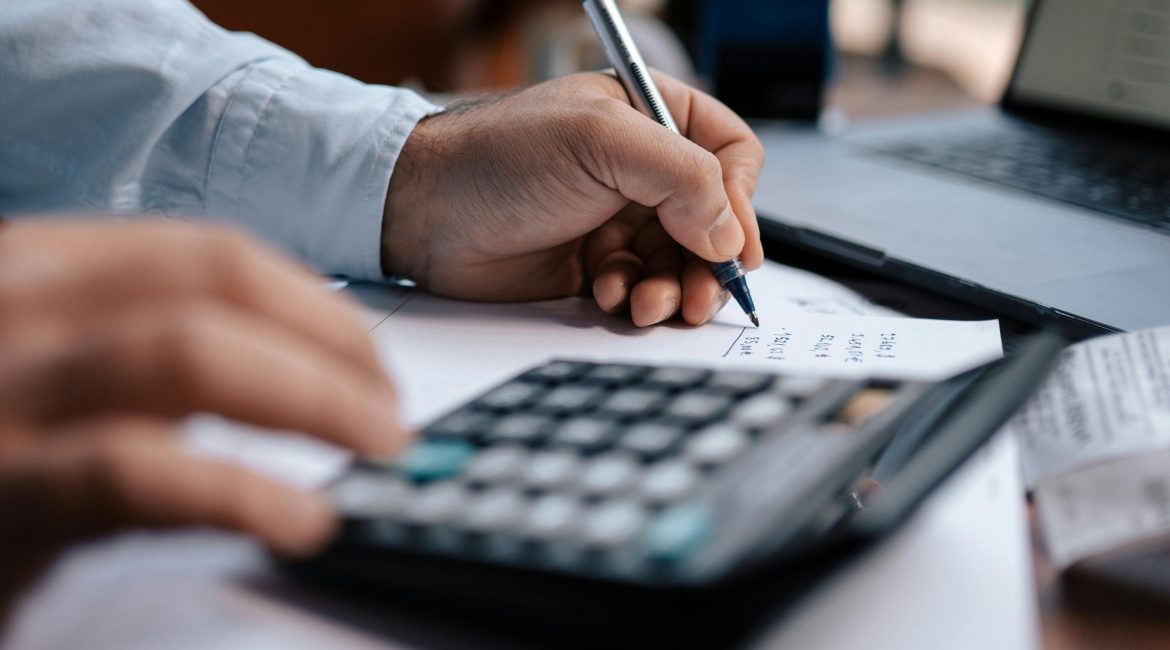 Persona revisando documentos financieros con calculadora y bolígrafo, representando servicios de asesoría fiscal y contable.