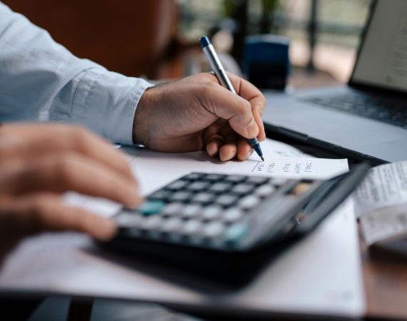 Persona revisando documentos financieros con calculadora y bolígrafo, representando servicios de asesoría fiscal y contable.