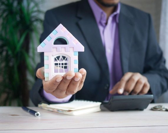 Abogado especializado en bienes raíces sosteniendo una casa en miniatura, simbolizando servicios legales en la compra, venta y gestión de propiedades.